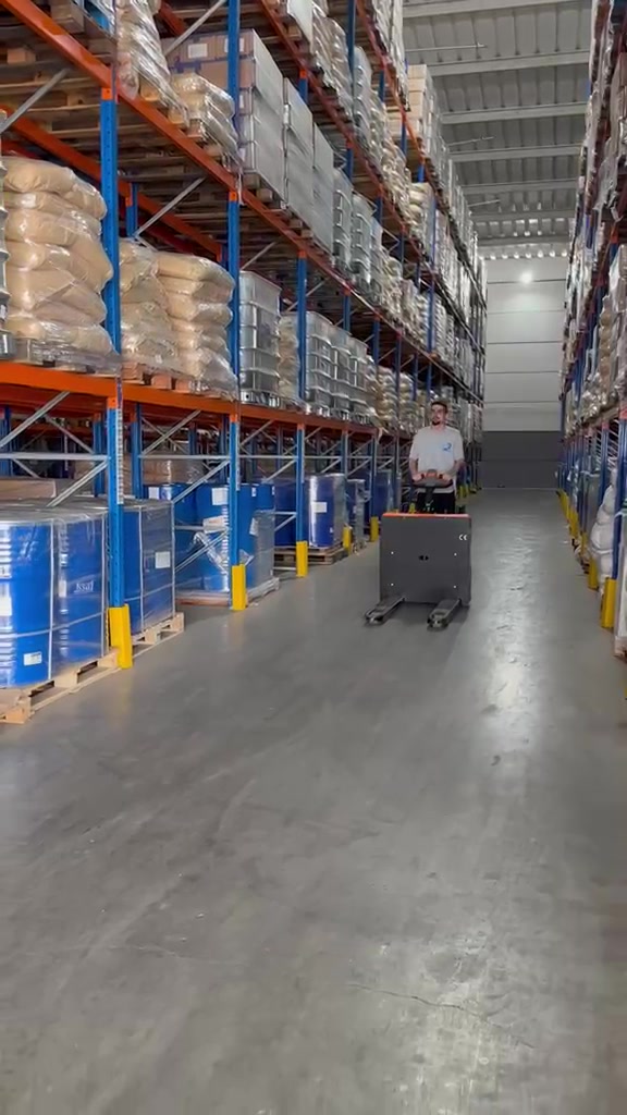 Operador conduzindo paleteira no corredor entre porta-paletes com mercadorias