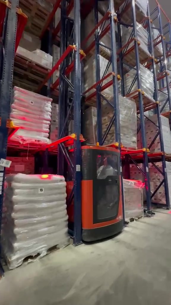 Operador em empilhadeira entre posições-palete com mercadorias armazenadas